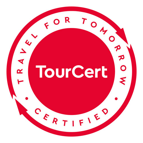 Rotes rundes Logo mit „TourCert“ in der Mitte, umgeben von „TRAVEL FOR TOMORROW CERTIFIED“ und zwei Pfeilen im Kreis.